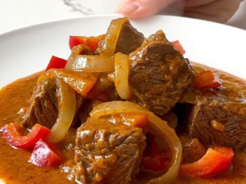 Crockpot beef paprikash with tender beef cubes, soft peppers and onions in a thick creamy paprika sauce on a white plate