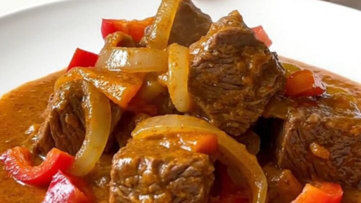 Crockpot beef paprikash with tender beef cubes, soft peppers and onions in a thick creamy paprika sauce on a white plate