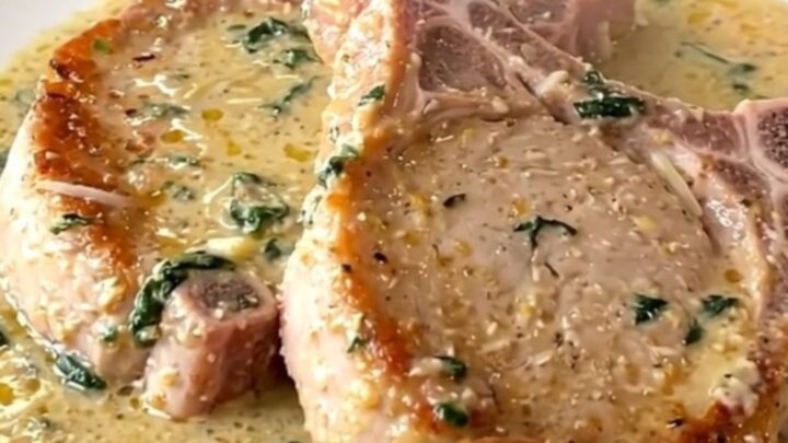 Boneless pork chops in thick creamy parmesan sauce with wilted spinach, served steaming on a white plate