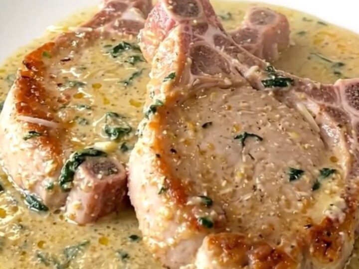 Boneless pork chops in thick creamy parmesan sauce with wilted spinach, served steaming on a white plate