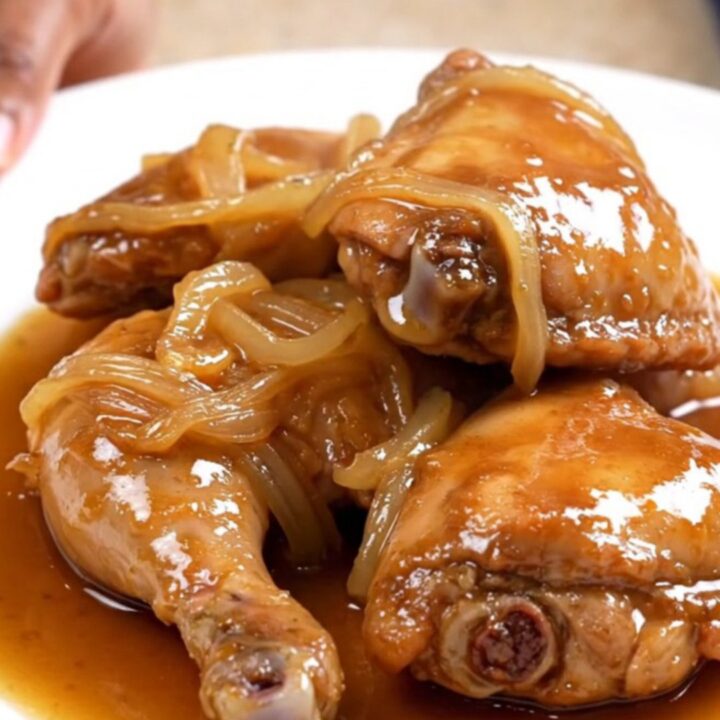 Slow cooker sweet tea chicken thighs with onions and glossy amber sauce on a white plate