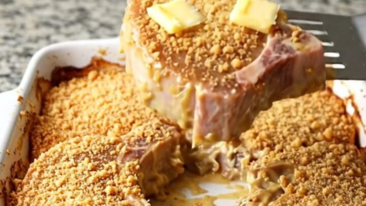Baked pork chops in a white ceramic dish under golden buttery cracker crumbs with bubbling creamy sauce at the edges
