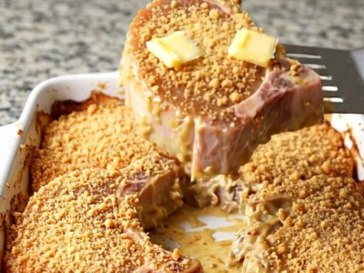 Baked pork chops in a white ceramic dish under golden buttery cracker crumbs with bubbling creamy sauce at the edges