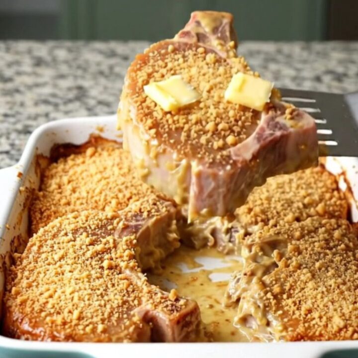 Baked pork chops in a white ceramic dish under golden buttery cracker crumbs with bubbling creamy sauce at the edges