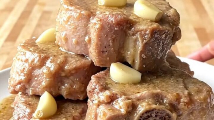 Fork-tender crockpot pork roast chunks on a white plate under thick creamy gravy with softened garlic cloves