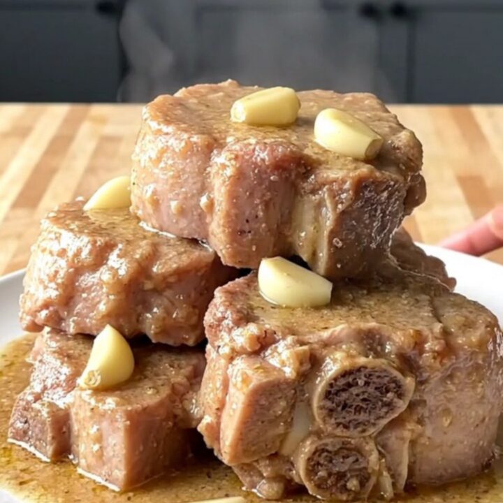 Fork-tender crockpot pork roast chunks on a white plate under thick creamy gravy with softened garlic cloves