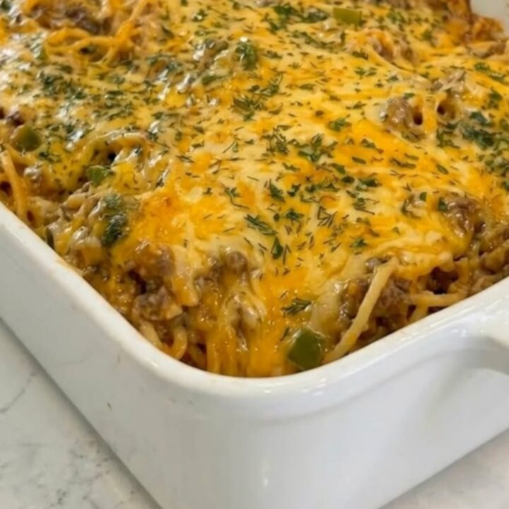 A spatula lifting a cheesy portion of taco spaghetti casserole from a white baking dish