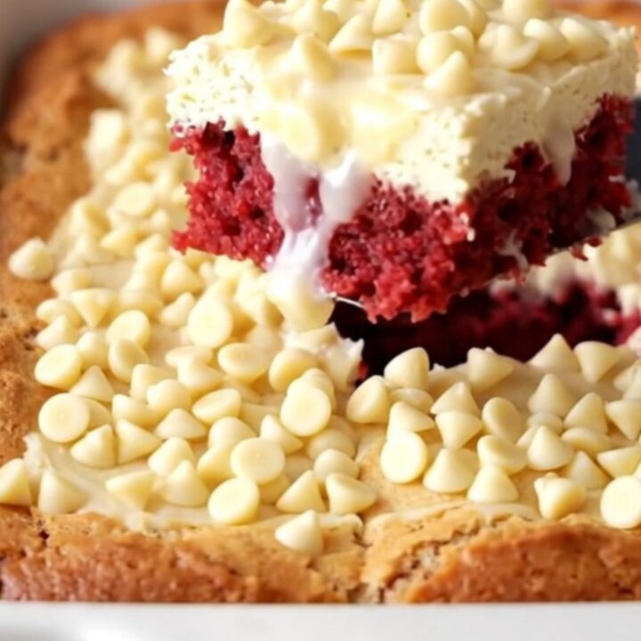 Baked red velvet gooey butter cake with pale golden top and white chocolate chips in a white ceramic dish