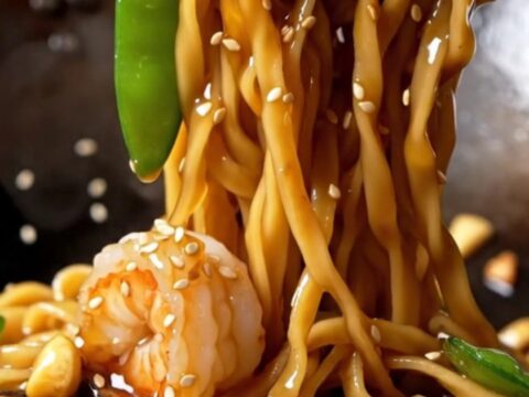 Glossy honey garlic shrimp lo mein with caramelized shrimp, snow peas, shiitakes, and sesame seeds lifted high from a skillet