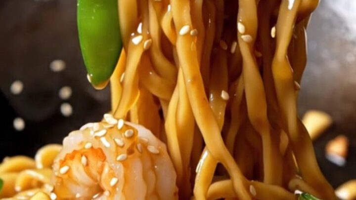 Glossy honey garlic shrimp lo mein with caramelized shrimp, snow peas, shiitakes, and sesame seeds lifted high from a skillet