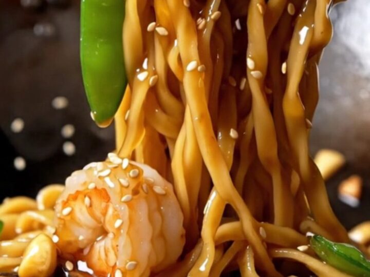 Glossy honey garlic shrimp lo mein with caramelized shrimp, snow peas, shiitakes, and sesame seeds lifted high from a skillet