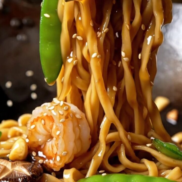 Glossy honey garlic shrimp lo mein with caramelized shrimp, snow peas, shiitakes, and sesame seeds lifted high from a skillet