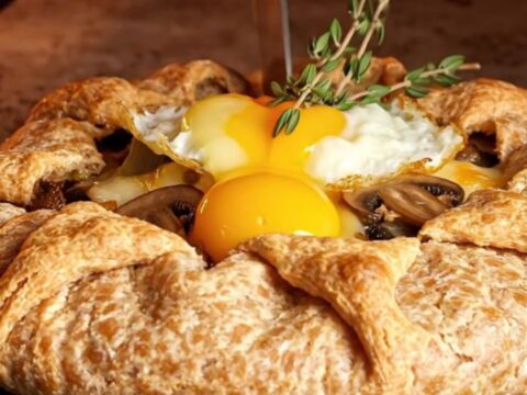 Rustic buckwheat galette with mushrooms, leeks, and blistered gruyere sliced on a dark slate board