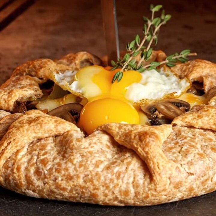 Rustic buckwheat galette with mushrooms, leeks, and blistered gruyere sliced on a dark slate board