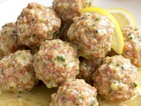 Turkey meatballs coated in creamy lemon herb sauce with soft lemon slices on a white round plate, steam rising