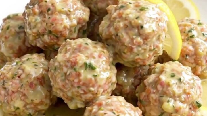 Turkey meatballs coated in creamy lemon herb sauce with soft lemon slices on a white round plate, steam rising