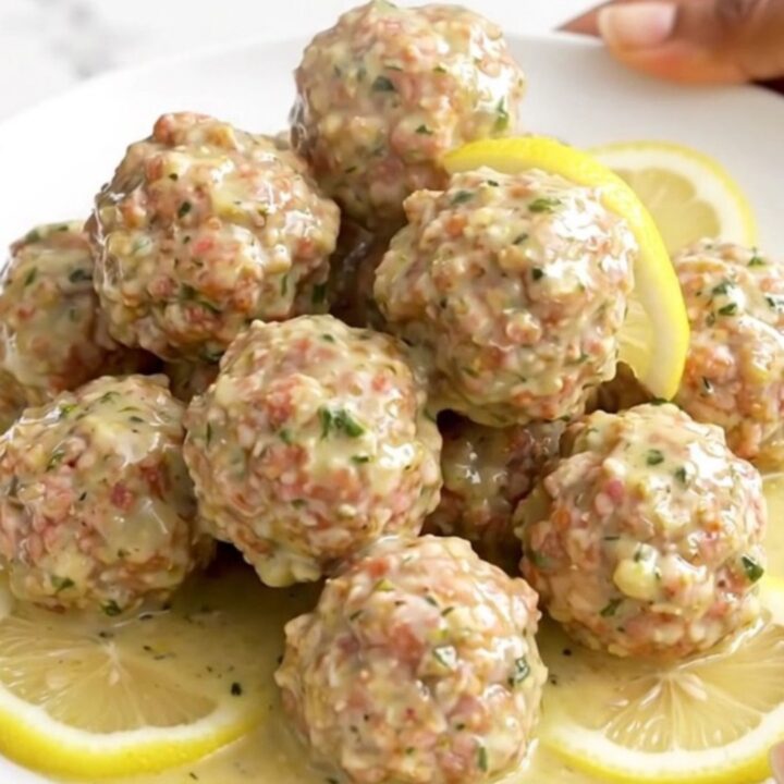 Turkey meatballs coated in creamy lemon herb sauce with soft lemon slices on a white round plate, steam rising