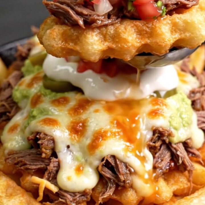 Skillet of loaded birria waffle fries with a molten Chihuahua cheese pull, pickled jalapeños and guacamole