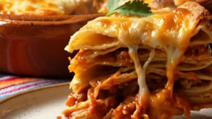 Tall square of pastel azteca Mexican tortilla lasagna with stretchy melted Oaxaca cheese and red guajillo chicken layers