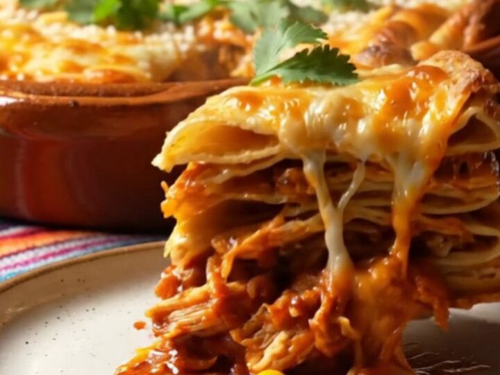 Tall square of pastel azteca Mexican tortilla lasagna with stretchy melted Oaxaca cheese and red guajillo chicken layers