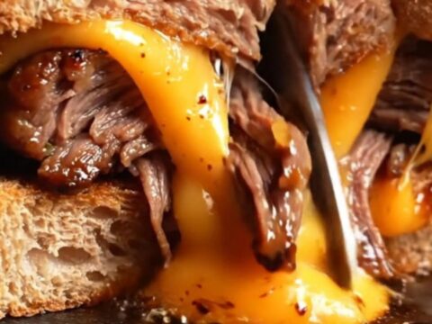 Diagonally sliced short rib grilled cheese with melted smoked Gouda and magenta pickled onions on golden sourdough