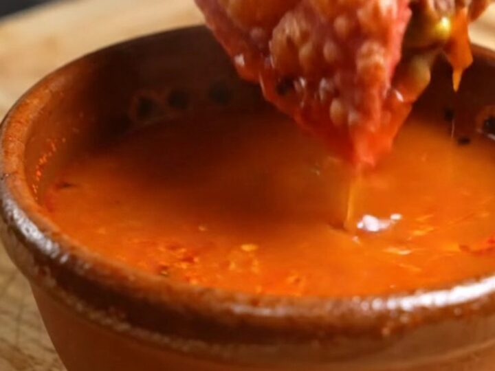 A birria mulita cut in half, red crispy tortillas stretching with melted Oaxaca cheese, beef birria and guacamole inside