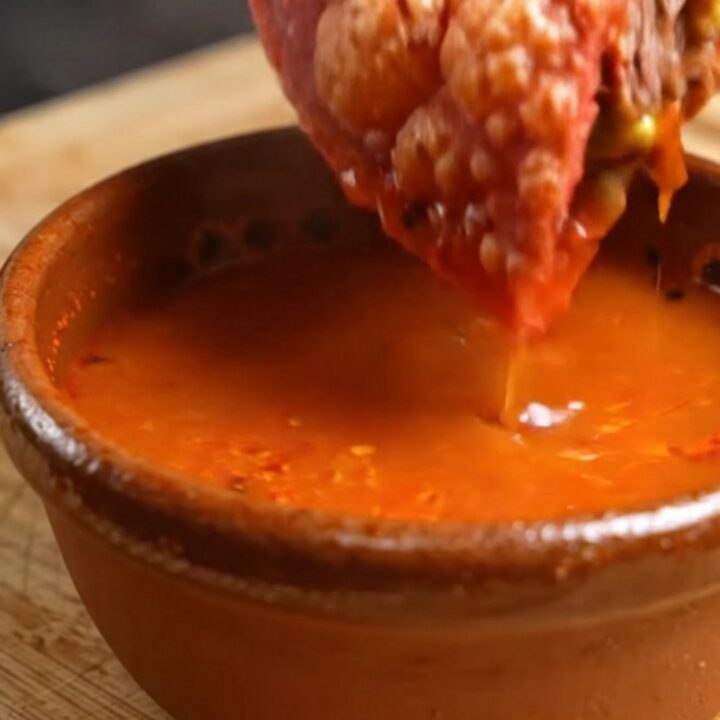 A birria mulita cut in half, red crispy tortillas stretching with melted Oaxaca cheese, beef birria and guacamole inside