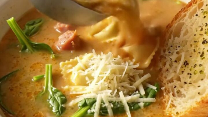 Slow-cooker creamy tortellini soup with Italian sausage crumbles and spinach in a deep bowl topped with grated parmesan