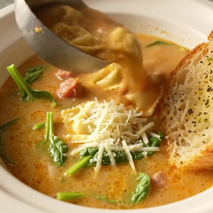 Slow-cooker creamy tortellini soup with Italian sausage crumbles and spinach in a deep bowl topped with grated parmesan