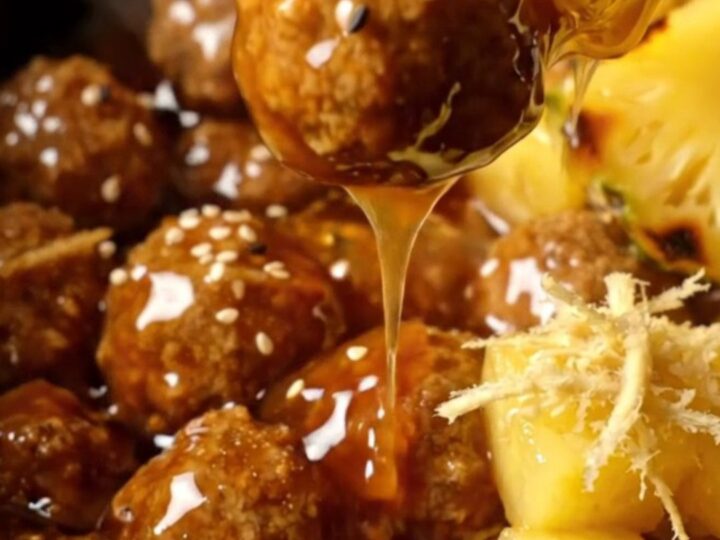 Glossy amber teriyaki-glazed pork meatballs with charred pineapple cubes and black and white sesame seeds in a slow cooker