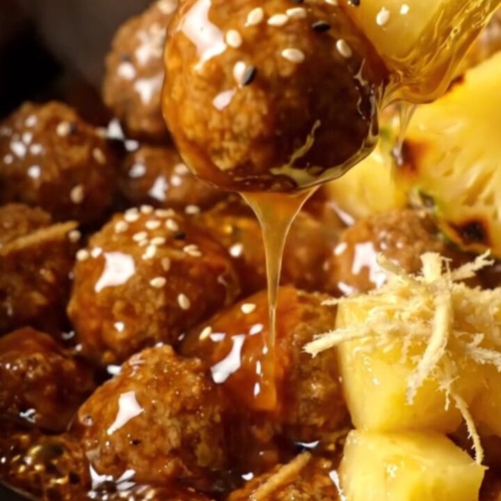 Glossy amber teriyaki-glazed pork meatballs with charred pineapple cubes and black and white sesame seeds in a slow cooker