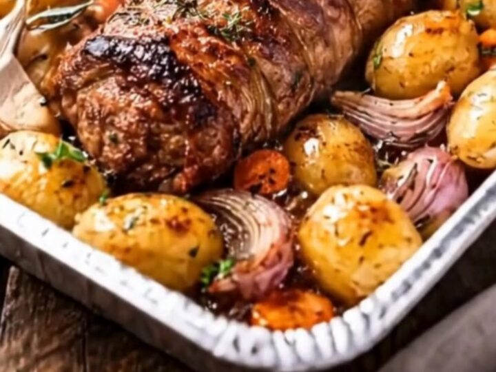 Rôti de porc doré reposant sur des grenailles dorées et des oignons rouges caramélisés dans un plat à rôtir, fumant
