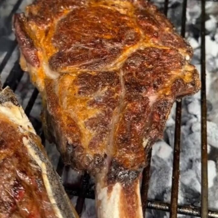 Thick bone-in ribeye steak on cast-iron grill grates over white-hot coals with a golden charred crust