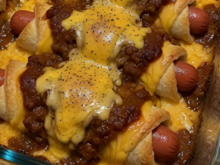 Chili cheese dog crescent rolls in a glass baking dish, smothered in beef chili with bubbling cheddar and cracked black