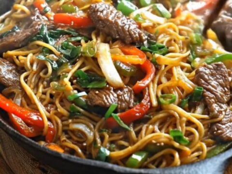 Steaming skillet of Mongolian beef noodles with flank steak, bell peppers and scallions in glossy sauce
