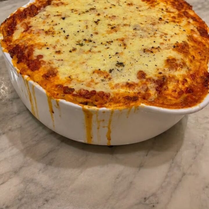 Golden-brown baked lasagna in a white ceramic dish with melted cheese bubbling on top