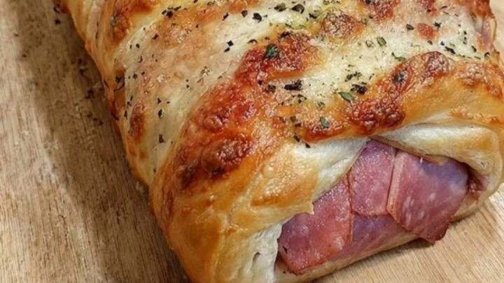 Golden-crusted ham and cheese stromboli sprinkled with herbs and parmesan on a wooden cutting board