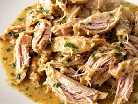 Shredded creamy French herb goat cheese chicken in a slow cooker, glossy sauce with leeks and herbs