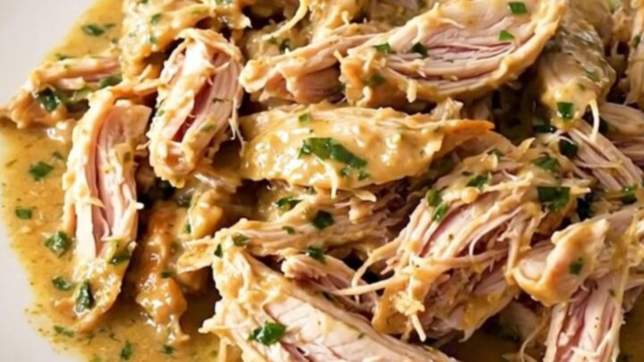 Shredded creamy French herb goat cheese chicken in a slow cooker, glossy sauce with leeks and herbs