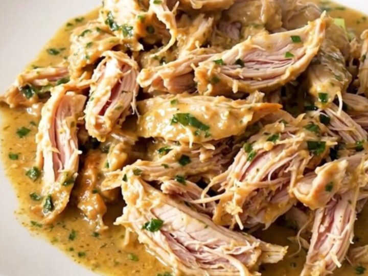 Shredded creamy French herb goat cheese chicken in a slow cooker, glossy sauce with leeks and herbs