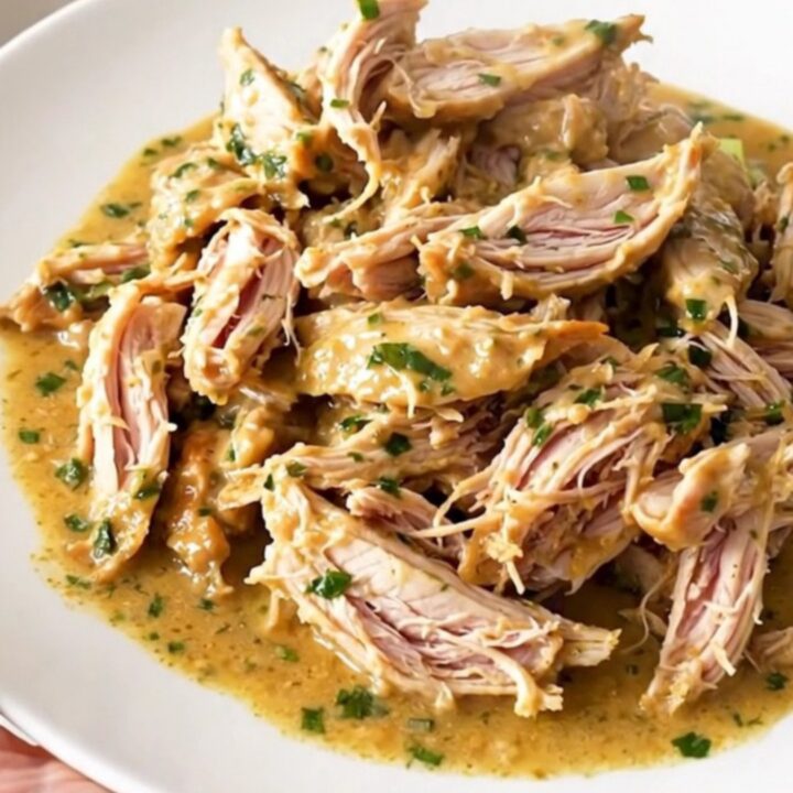 Shredded creamy French herb goat cheese chicken in a slow cooker, glossy sauce with leeks and herbs