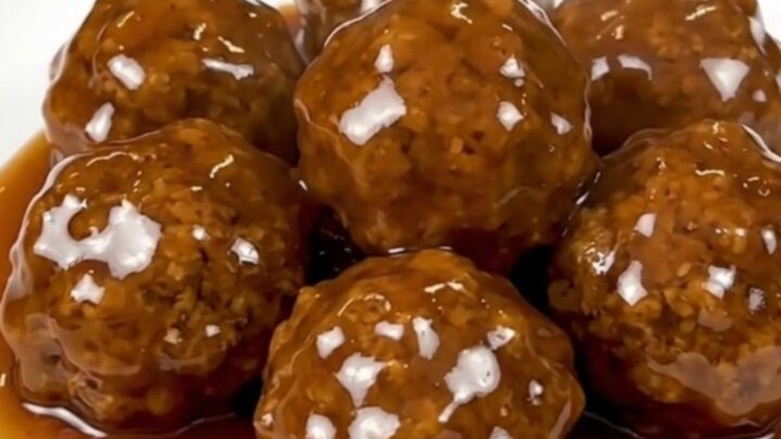 Glossy honey garlic chicken meatballs piled on a white plate, steaming and coated in sticky amber glaze