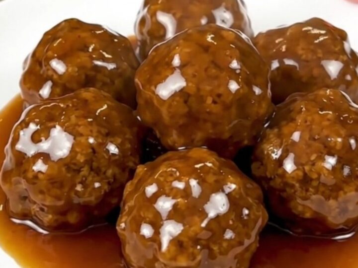 Glossy honey garlic chicken meatballs piled on a white plate, steaming and coated in sticky amber glaze