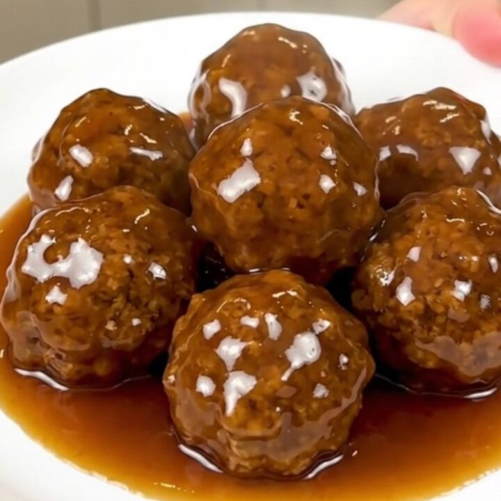 Glossy honey garlic chicken meatballs piled on a white plate, steaming and coated in sticky amber glaze