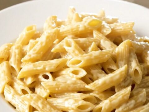 Creamy four cheese penne steaming in a black oval slow cooker on a white speckled quartz countertop