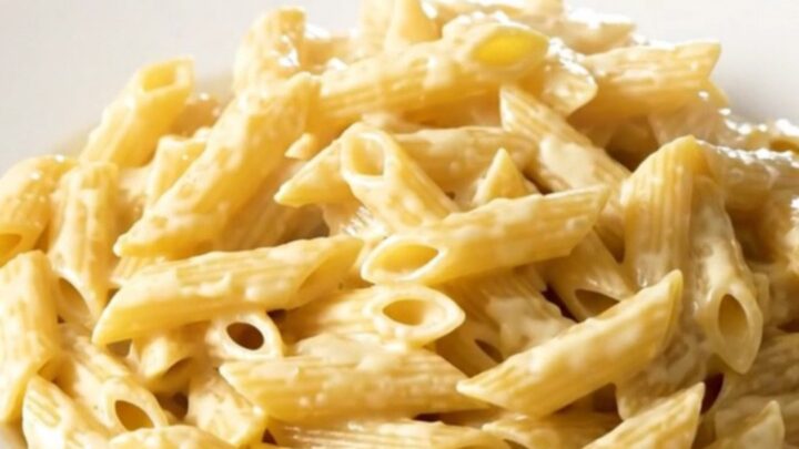 Creamy four cheese penne steaming in a black oval slow cooker on a white speckled quartz countertop