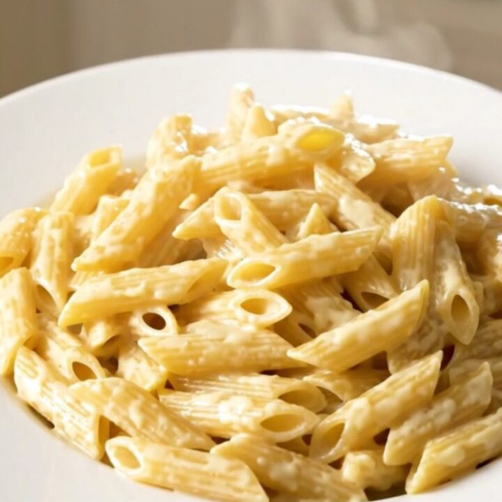 Creamy four cheese penne steaming in a black oval slow cooker on a white speckled quartz countertop