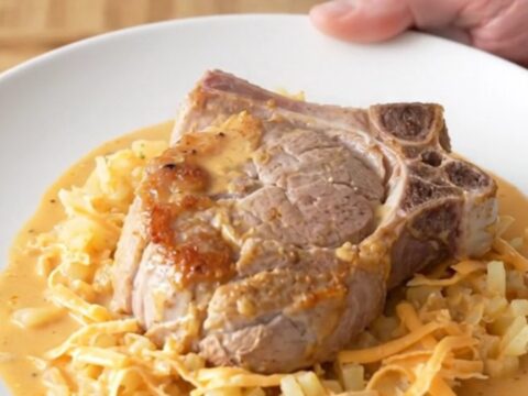 Slow cooker cheesy hash brown pork chops, soft braised chop over creamy cheesy shredded potatoes with steam rising