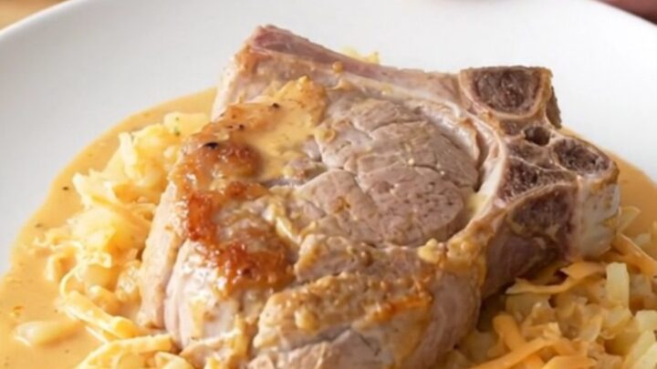 Slow cooker cheesy hash brown pork chops, soft braised chop over creamy cheesy shredded potatoes with steam rising