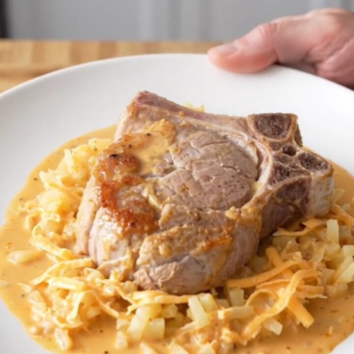 Slow cooker cheesy hash brown pork chops, soft braised chop over creamy cheesy shredded potatoes with steam rising